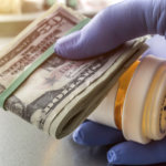 Doctor holding a pill bottle as well as rolled dollar bills.
