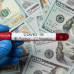 Gloved hand holding covid-19 vial over money.