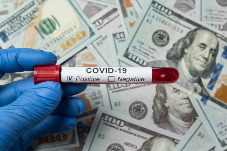 Gloved hand holding covid-19 vial over money.